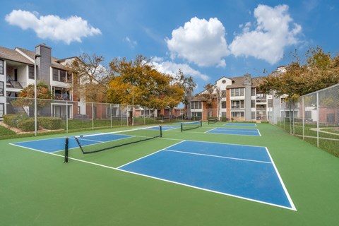 A tennis court surrounded by a fence and buildings.