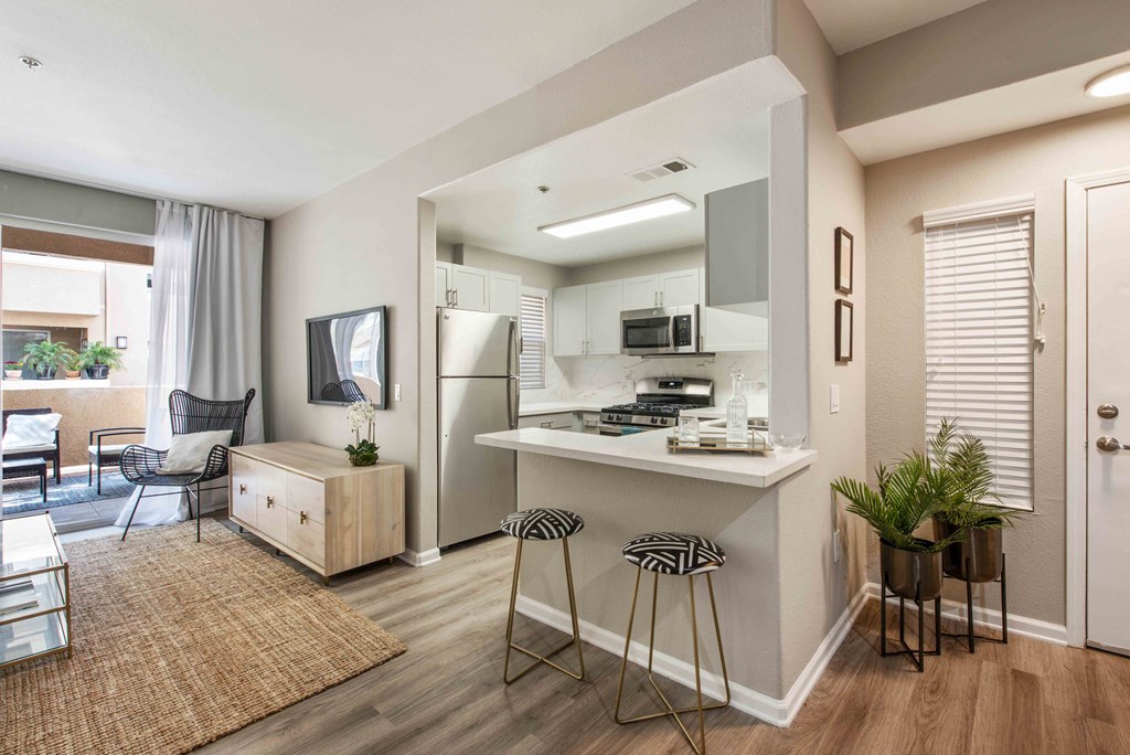 Camarillo, CA Apartments with In-Unit Washer and Dryer - Allure - Interior Living Area With Connected Private Patio and Connected Kitchen with Wood-Style Flooring, Stainless Steel refrigerator, Oven, White Cabinetry, White Countertop, and Bar Stool Seating.