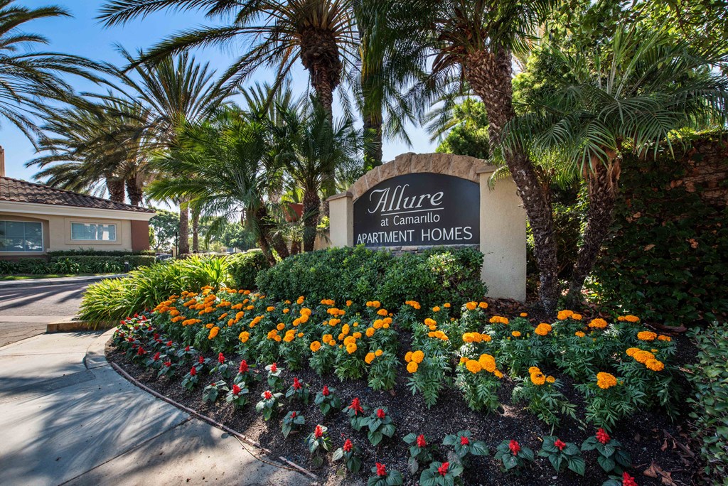 a sign in front of a garden with flowers and palm trees