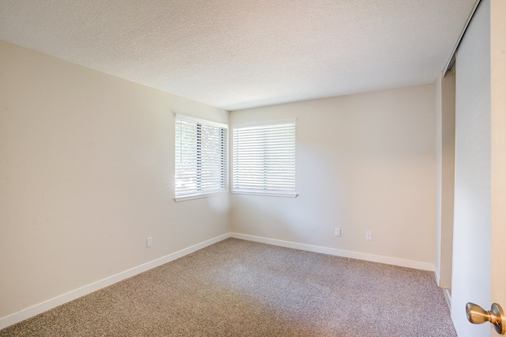 a bedroom with beige carpet and two windows