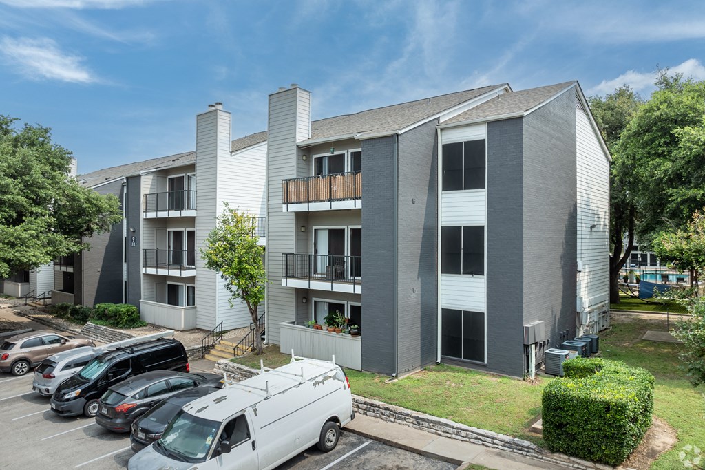 an image of an apartment building with cars parked in a parking lot