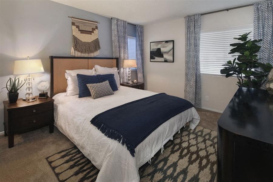 2 BR Apartments in Rancho Cucamonga CA - Creekside Alta Loma - Bedroom with Bed, Nightstands, Lamps, Area Rug, Dresser, Blue Accent Wall, and Two Windows.