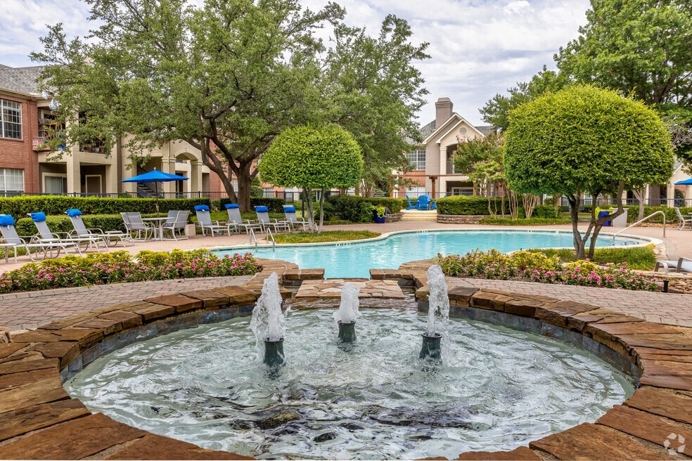 a fountain in front of a swimming pool with chairs and trees