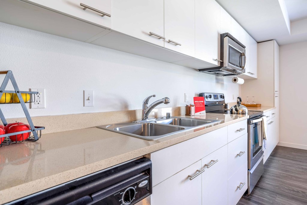 One Bedroom Apartments in Green Lake Seattle WA - Circa Green Lake - Kitchen with White Cabinets, Beige Countertops, and Stainless Steel Appliances.