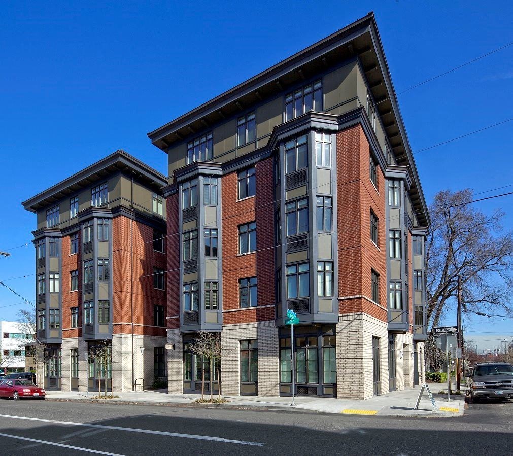 A red car is parked on the street in front of a multi-story building.