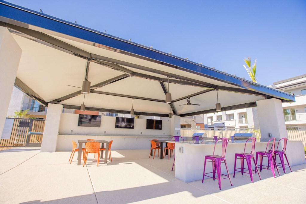 Gilbert, AZ Apartments - Outdoor Lounge With BBQ Grills, Chairs, Tables, Fans, And Three TV Screens.
