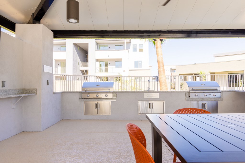 a patio with a table and chairs and two barbecue grills