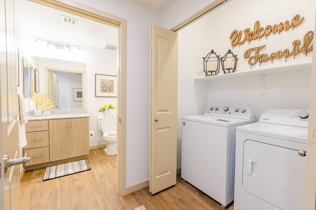 Three Bedroom Apartments in Gilbert AZ - Curve At Gilbert - Bathroom With Plank Flooring, Wood-Inspired Cabinets, A Large Vanity Mirror, And A Full-Sized In-Unit Washer And Dryer