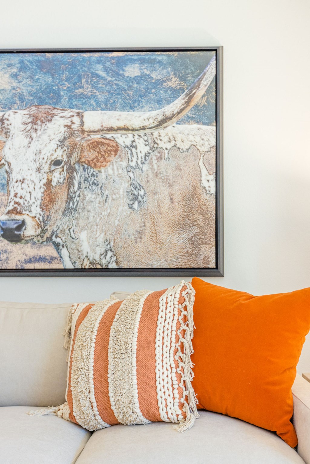 a white couch with an orange pillow and a painting of a cow