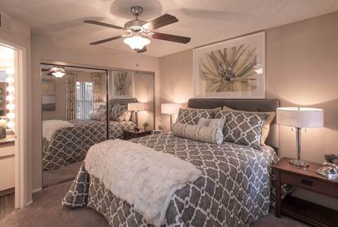 Ahwatukee, AZ, Apartments Near I-10 - Pacific Bay Club - Inviting Bedroom With Plush Bed, Patterned Bedding, Mirrored Closet Doors, Bedside Lamps, Ceiling Fan, And Neutral Wall Art.