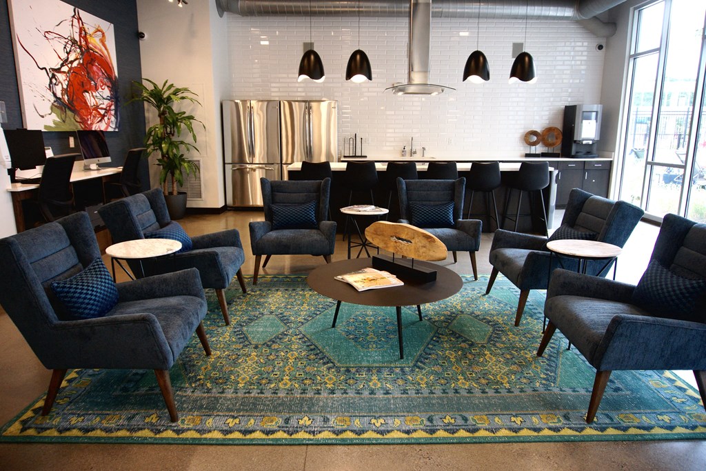 a lounge area with chairs and tables and a kitchen in the background