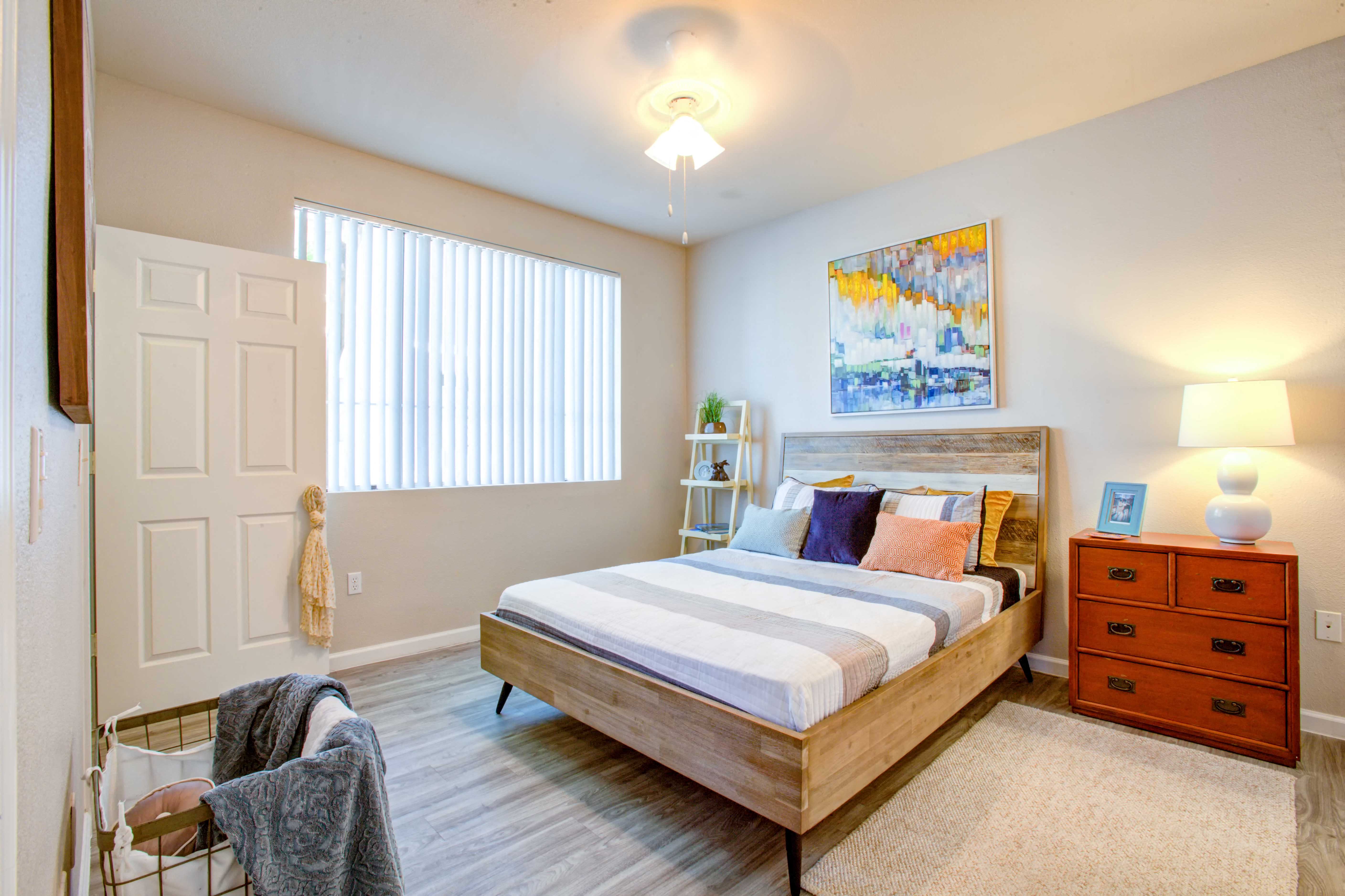 1 Bedroom Apartments in North Phoenix - Ironhorse at Tramonto - Bedroom with Wood-Style Flooring, Area Rug, Bed, Dresser/Nightstand, Lamps,Hamper, Storage Rack, and Large Window