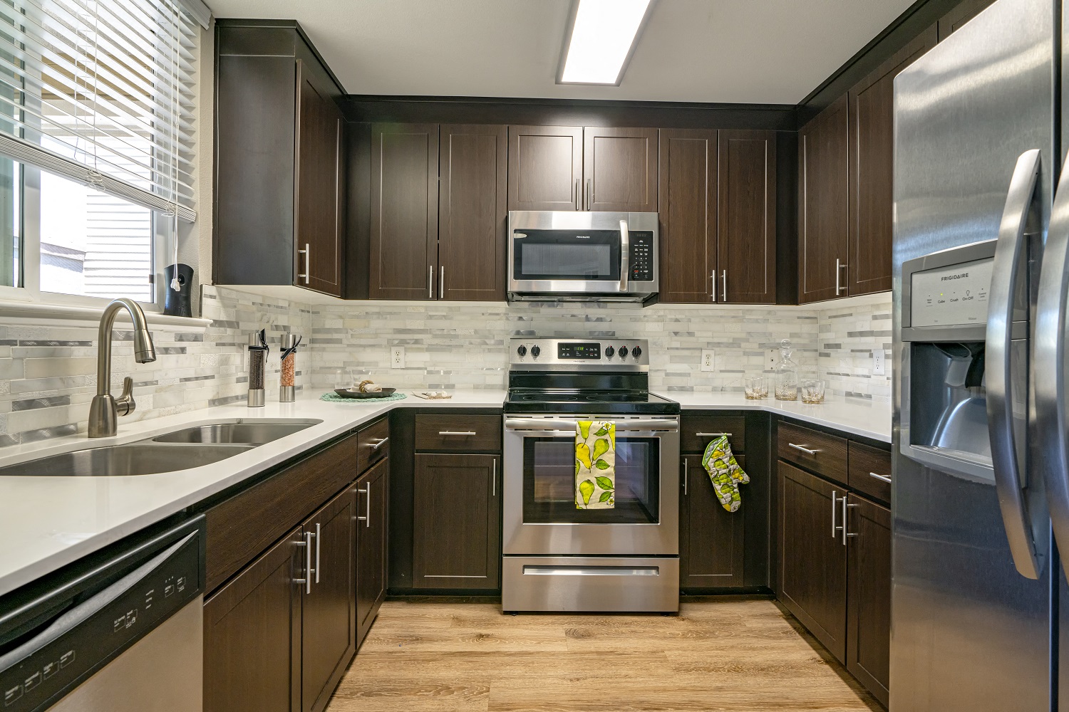 One-Bedroom Apartments in Walnut Creek, CA - Ivy Hill - Kitchen with Wood-Style Cabinetry, Stainless Steel Appliances, White Counters, and White/Grey Tile Backsplash