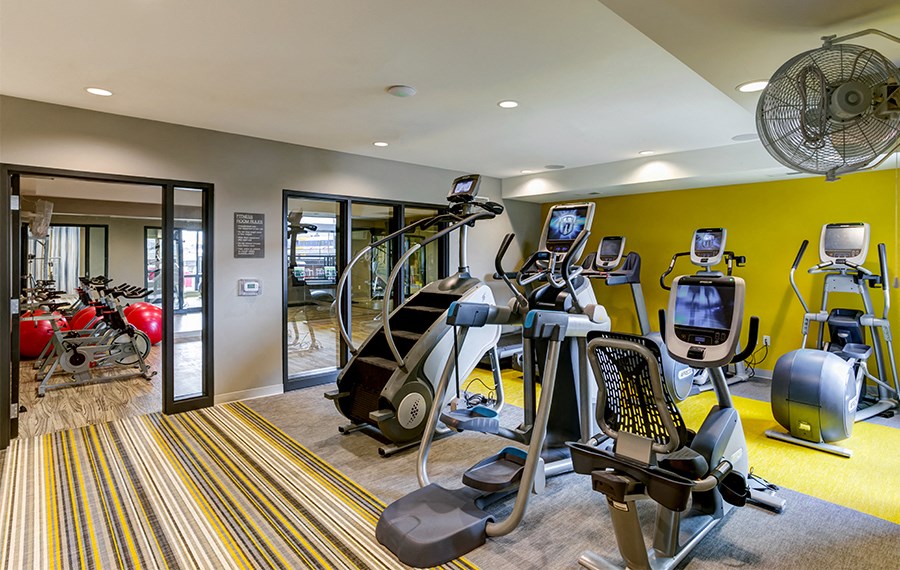 a gym with cardio equipment and weights in a building with yellow walls