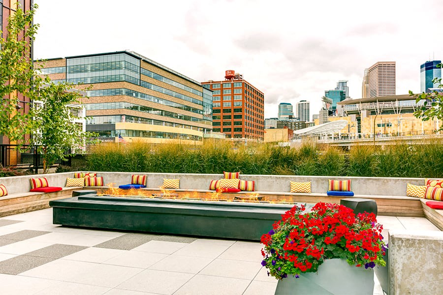A patio with a bench and a planter with red flowers.