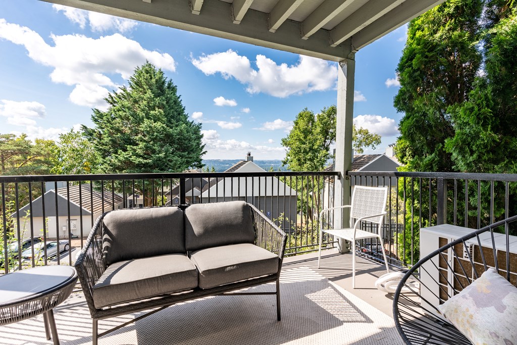 Mountain Park OR Apartments for Rent - MiLO at Mountain Park - Private Balcony with Patio Furniture and an Area Rug, Surrounded by a View of Trees and the Apartment Building.