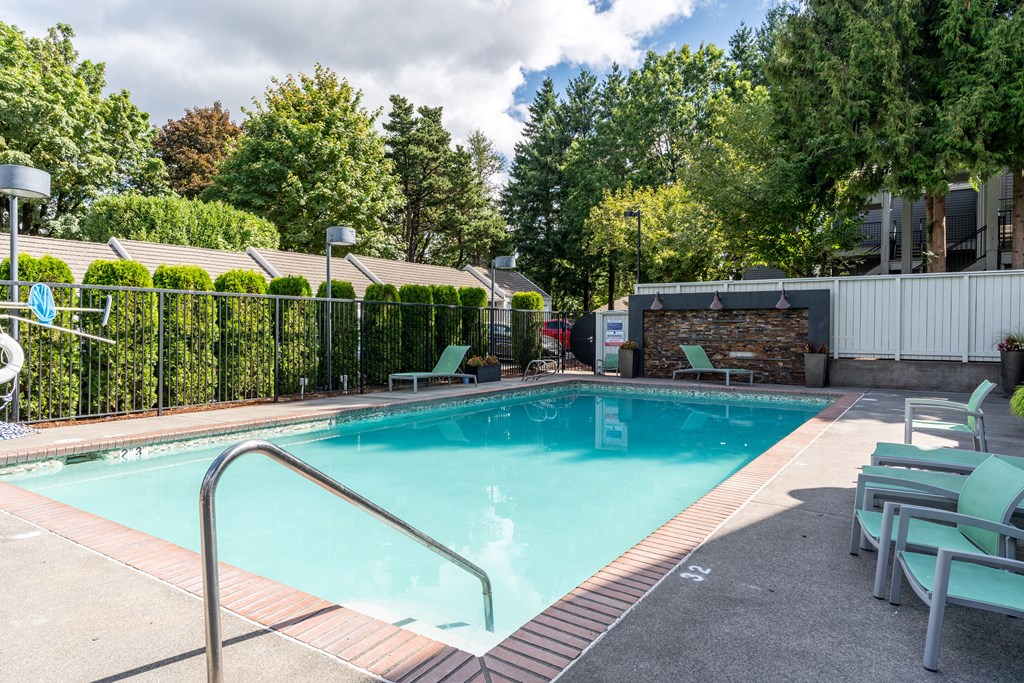 a swimming pool with lounge chairs and trees in the background