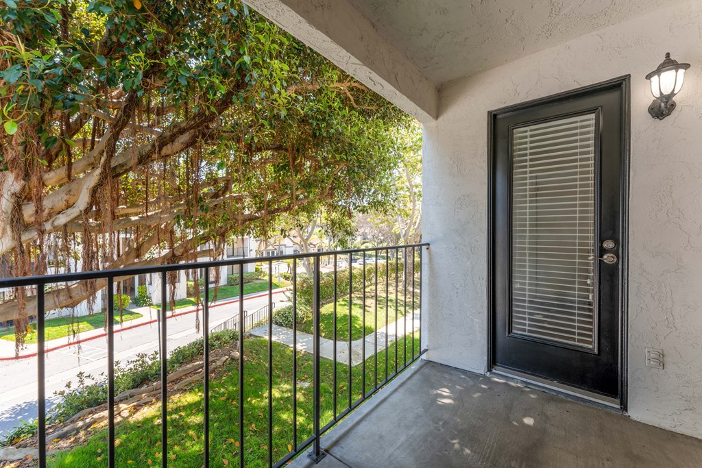 a balcony with a black railing and a door and a tree