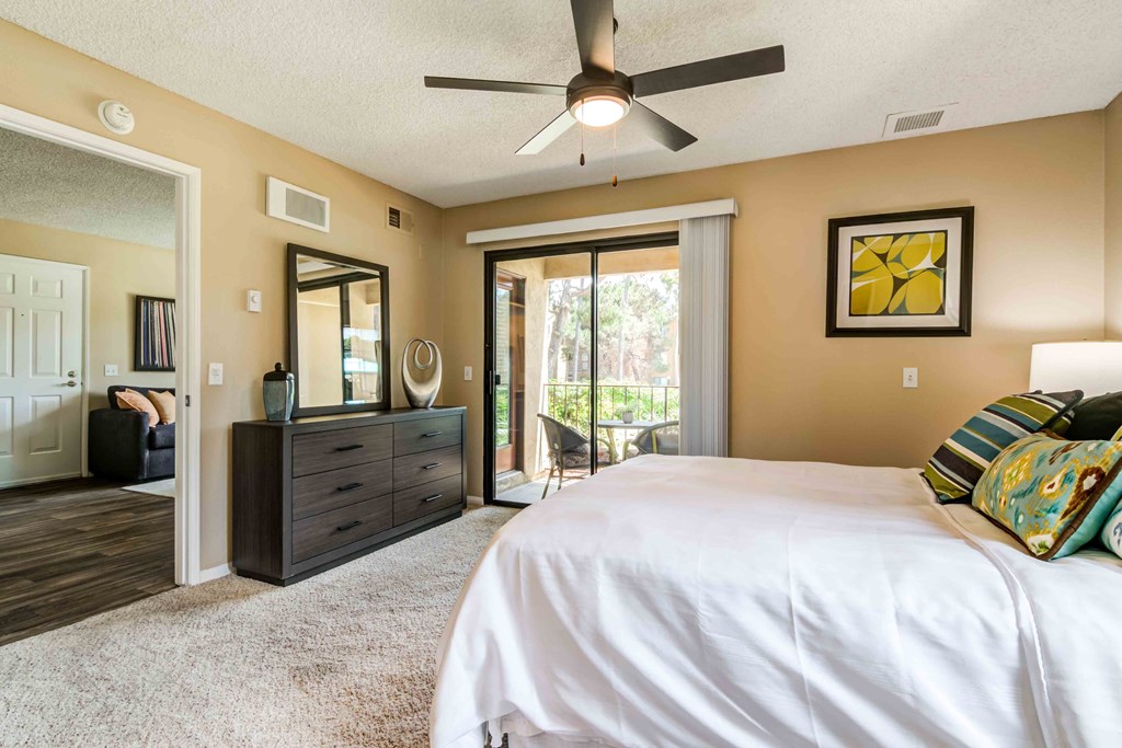 Pet-Friendly Apartments in La Jolla, CA - Mirada at La Jolla Colony - Bedroom with Direct Patio Access, a Ceiling Fan, and Plush Carpet Flooring