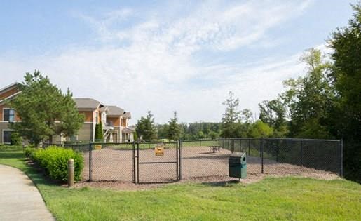 fenced dog park area with equipment next to sidewalk and apartment buildings