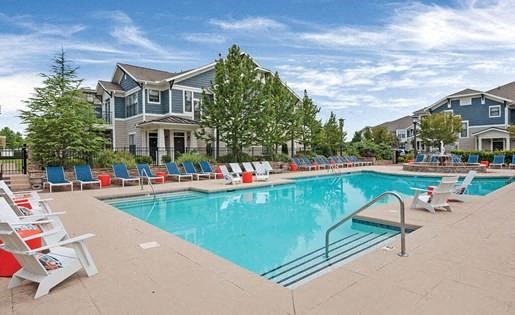 large swimming pool with lots of seating and apartment buildings in background