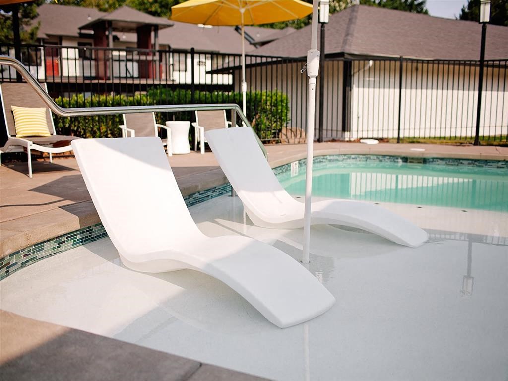 a pool with two white chairs and a poolside umbrella