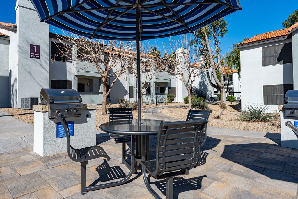 a patio with an umbrella and a table with chairs and a grill