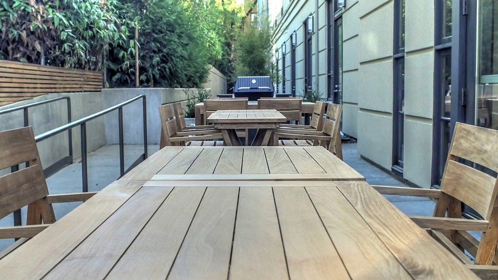 One-Bedroom Apartments in Nob Hill, Portland, OR - The Cordelia - BBQ Grilling Station with Wooden Tables, Chairs, and Greenery