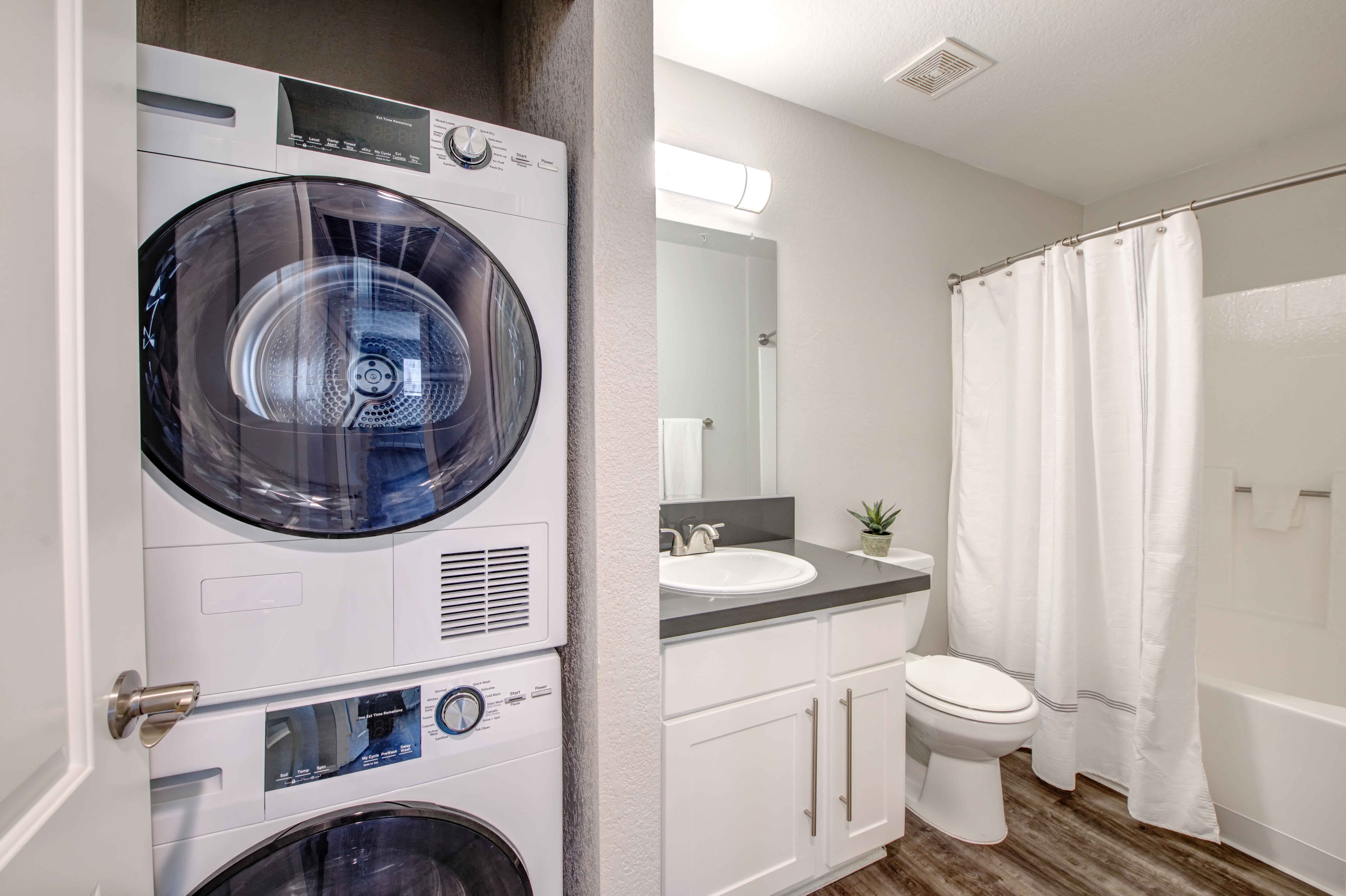 Apartments in San Clemente, CA - Rancho Del Mar - Bathroom with Hardwood-Inspired Flooring, a Toilet, a Shower, a Vanity with White Cabinets, and an In-Unit Washer/Dryer
