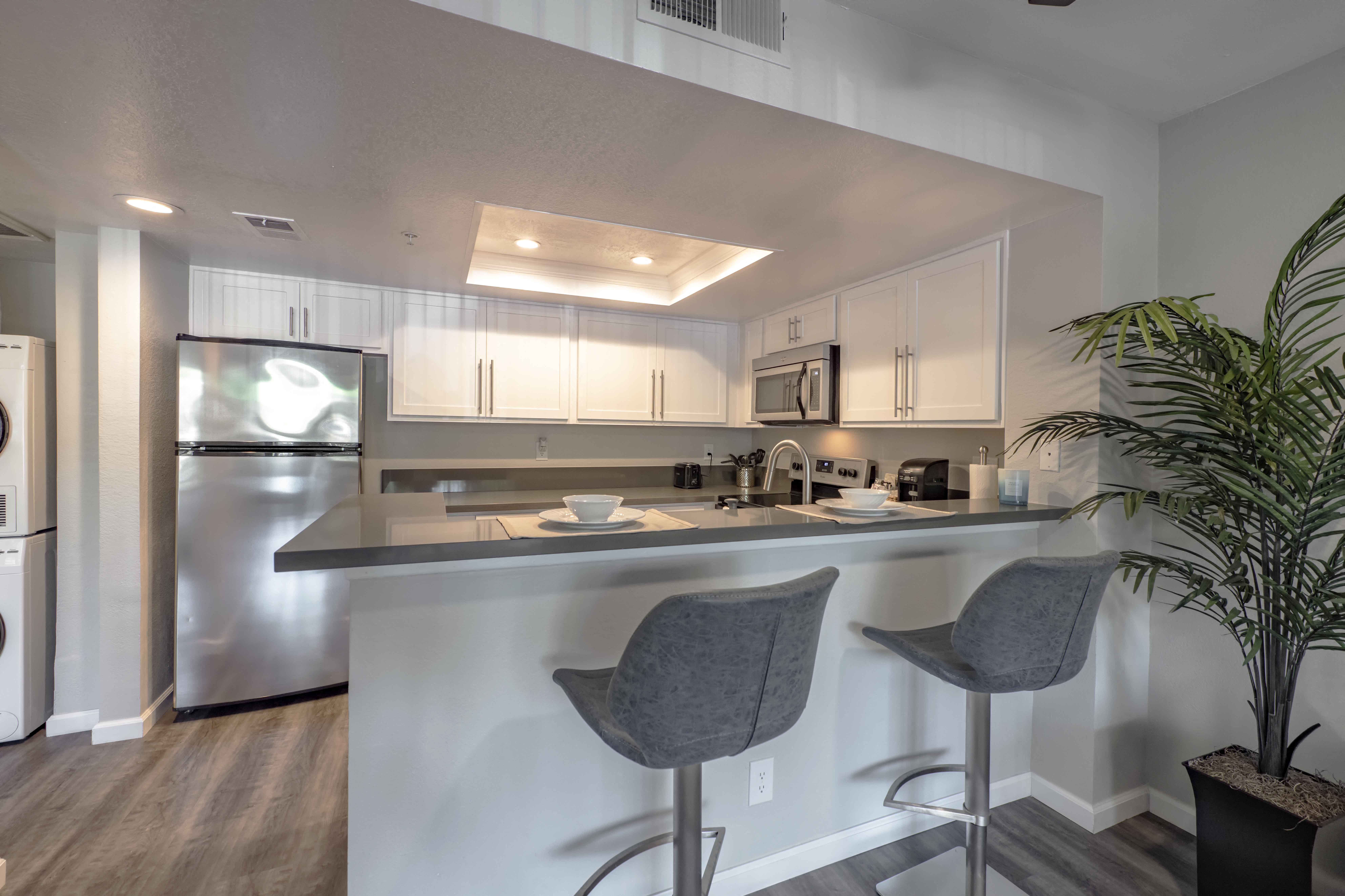One-Bedroom Apartments in San Clemente, CA - Rancho Del Mar - Modern Kitchen with White Cabinets, Stainless Steel Appliances, Grey Countertops, High Top Seating, and Stylish Decor