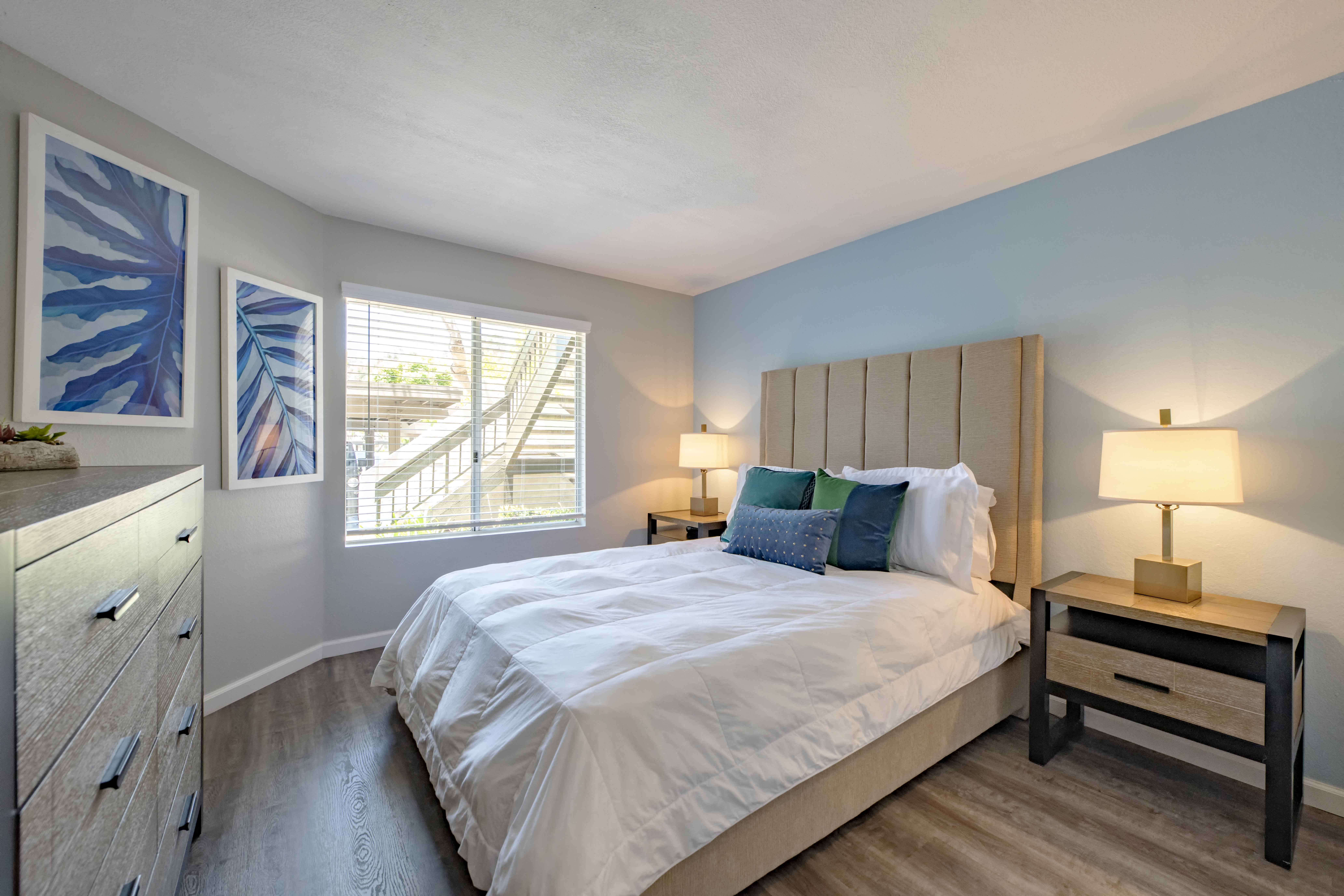 Apartments in San Clemente for Rent - Rancho Del Mar - Spacious Bedroom with Large Window, Wood-Style Flooring, and Light Blue Accent Wall