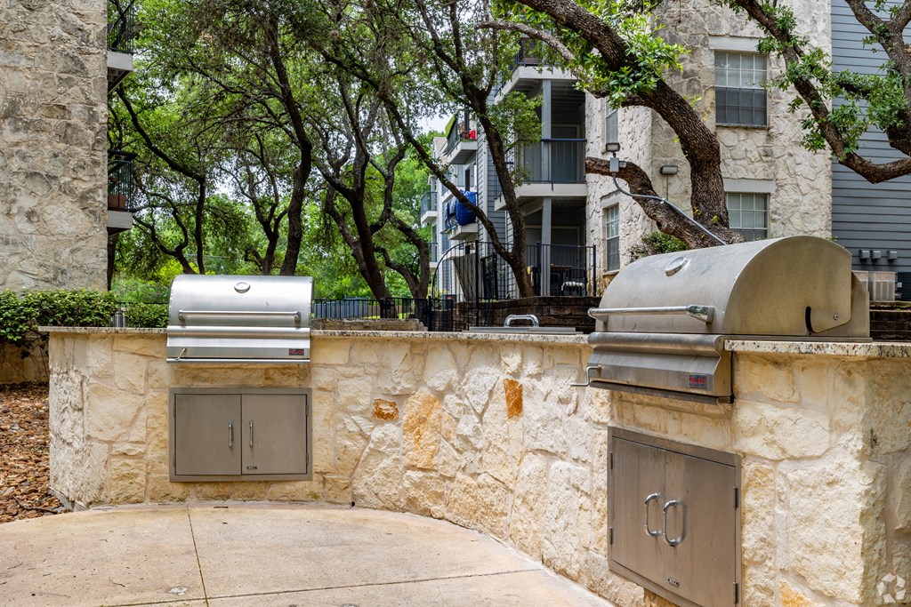 a stone retaining wall with two stainless steel barbecue grills in front of a house