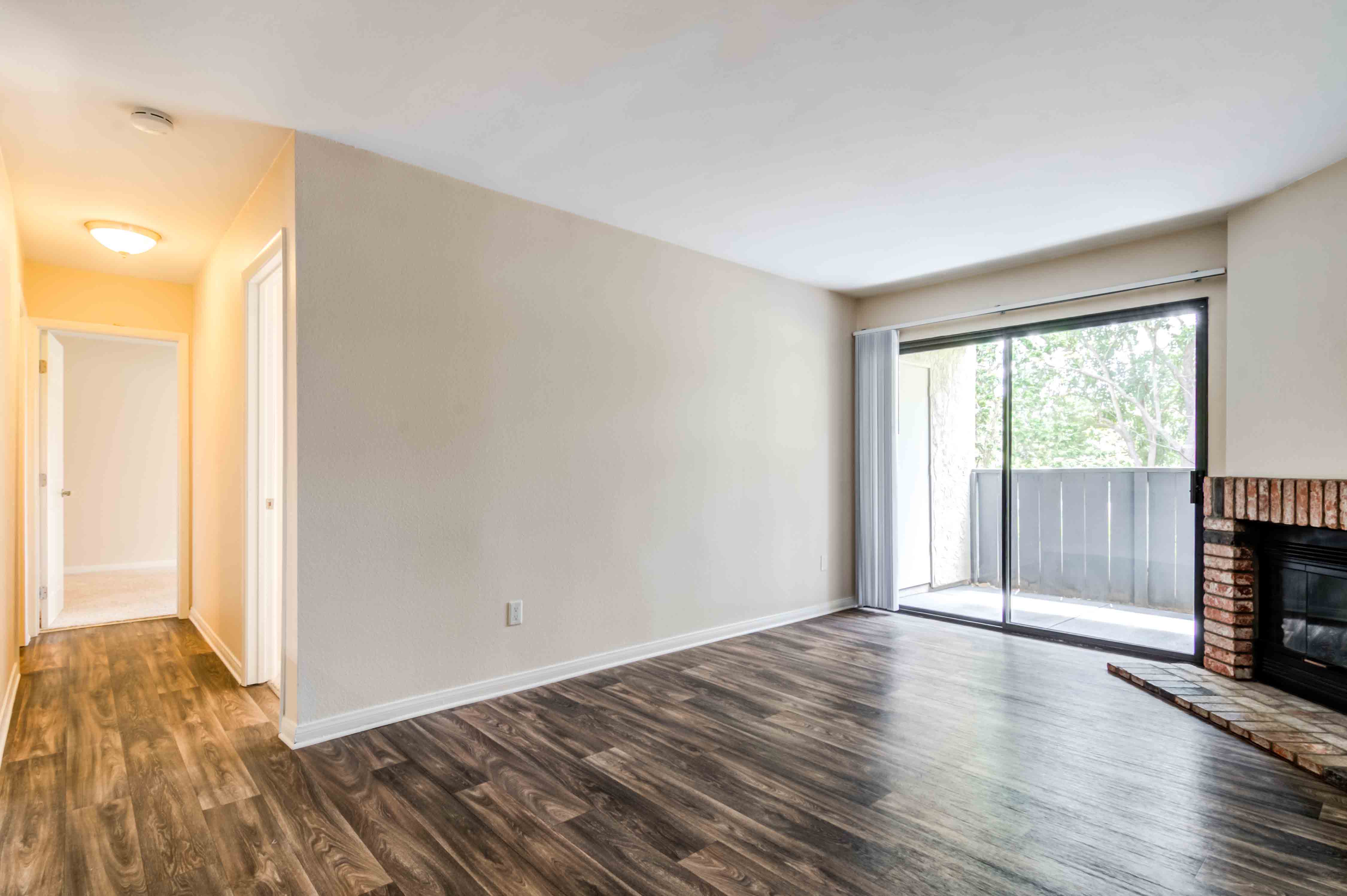 Dog-Friendly Apartments in Carlsbad, CA - Santa Fe Ranch - Living Room with a Wood Burning Fireplace, Wood-Style Flooring, and a Large Sliding Glass Door to a Private Patio/Balcony