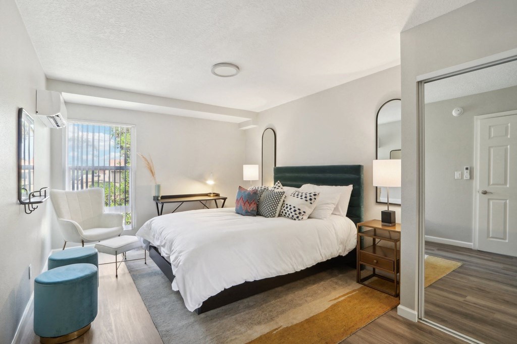 One-Bedroom Apartments in Van Nuys, CA - San Regis - Bedroom with Vinyl Plank Flooring, a Closet with Sliding Mirror Doors, and a Large Window