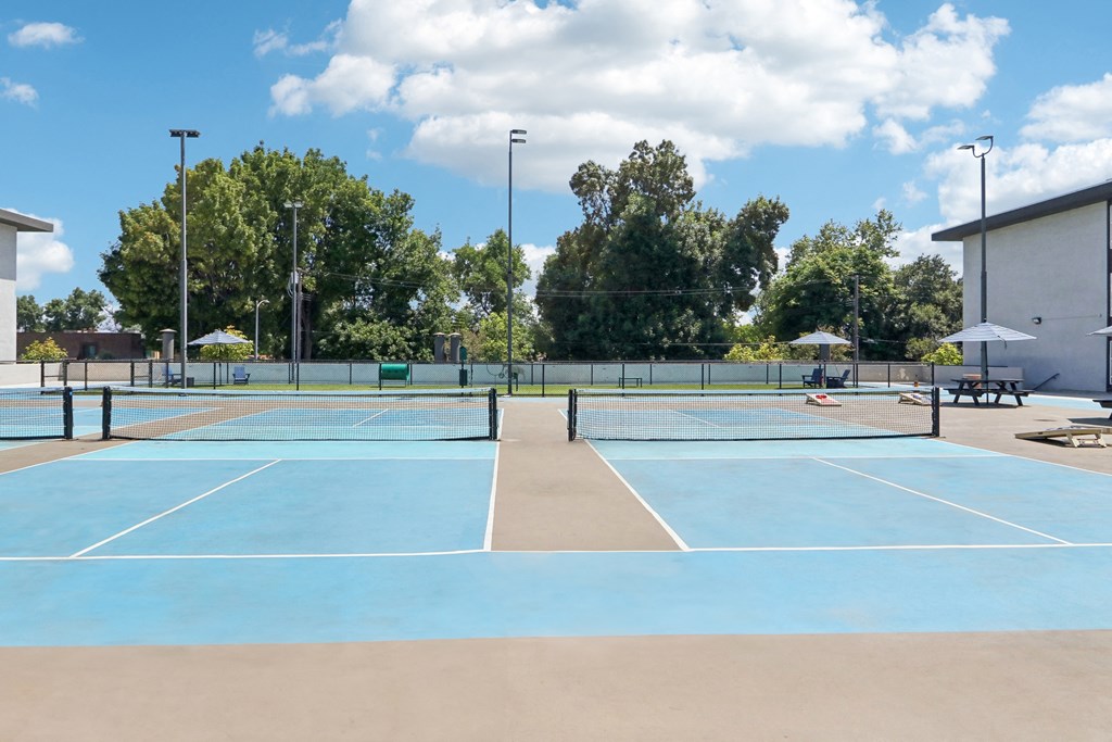 a tennis court with umbrellas and benches on a sunny day