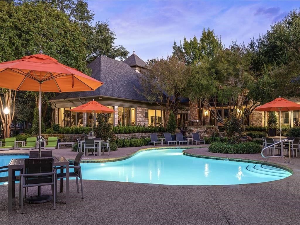 a swimming pool with tables and umbrellas at dusk