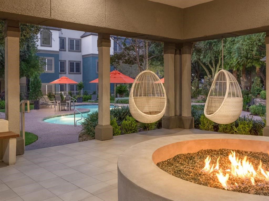 a fire pit with hanging hammocks next to a building with a pool