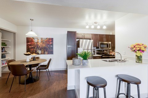 A kitchen with a table and chairs in the foreground and a kitchen in the background.