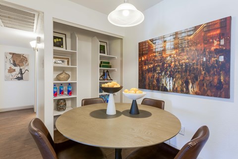 Dog-Friendly Apartments in Scottsdale, AZ - The Sycamore at Scottsdale - Dining Area With Round Table, Built-In Shelving, Pendant Light, Wall Art, And Warm Wood Style Flooring.