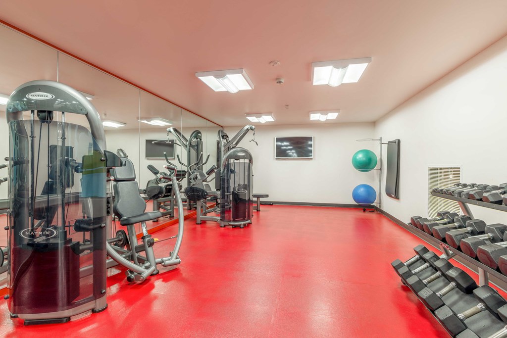 a gym with cardio machines and weights on a red floor