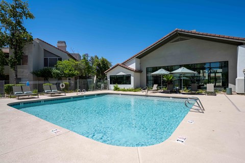 North Phoenix, AZ Luxury Apartments For Rent - Village At Lakewood - Outdoor Gated Pool Area With Lounge Seating, Umbrellas, And A View Of The Community Clubhouse.