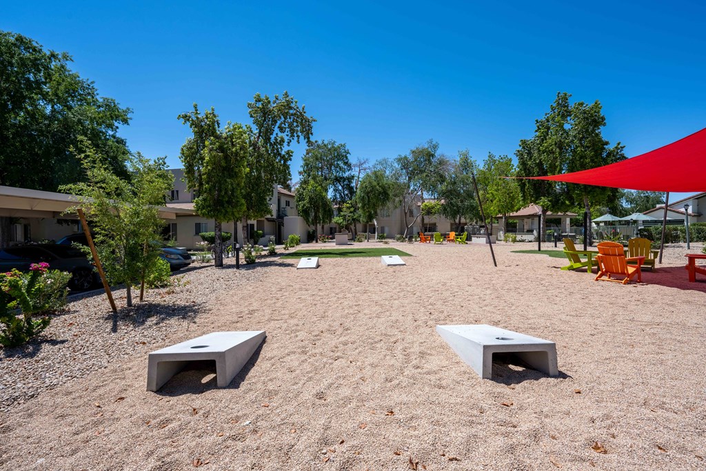 Two-Bedroom Apartments in Ahwatukee, Phoenix, AZ - Village at Lakewood - Outdoor Area with Cornhole Boards, Tall Trees, and a Red Canopy.