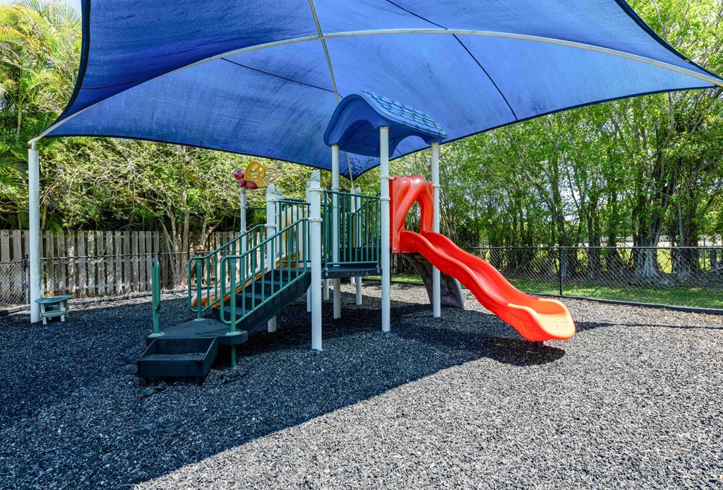 Apartments In Coconut Creek for Rent – Waterview at Coconut Creek – playground with a slide and a swing set under a blue umbrella