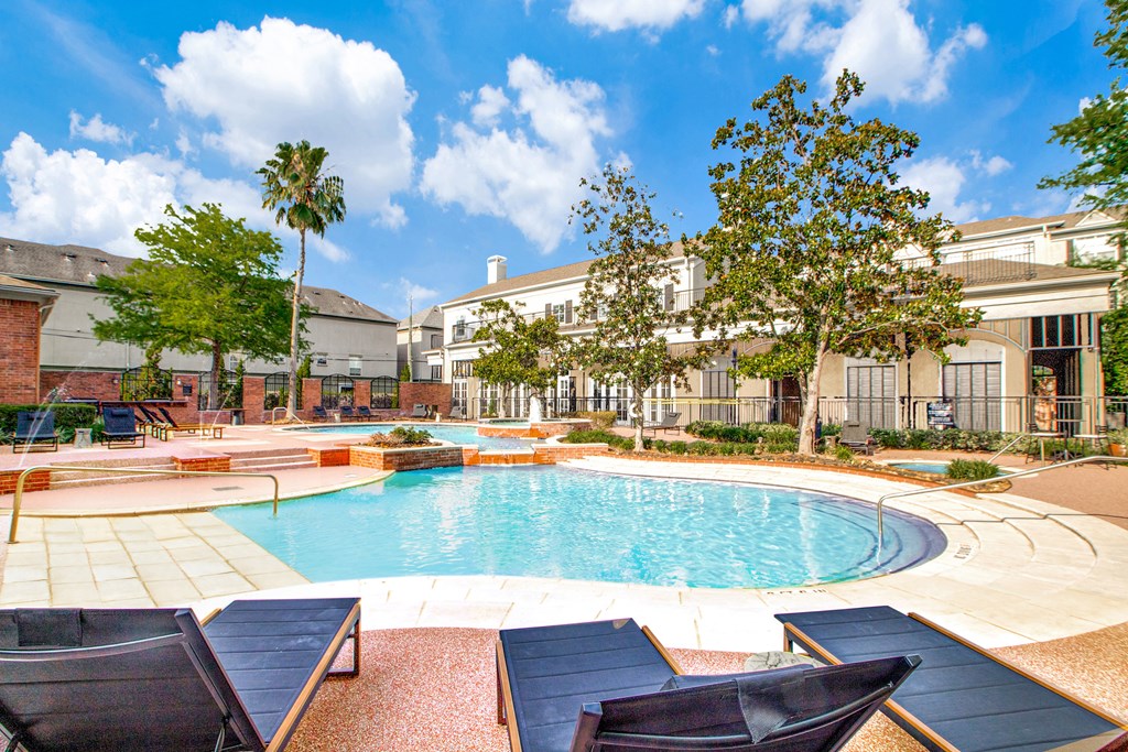 A pool surrounded by lounge chairs and trees.
