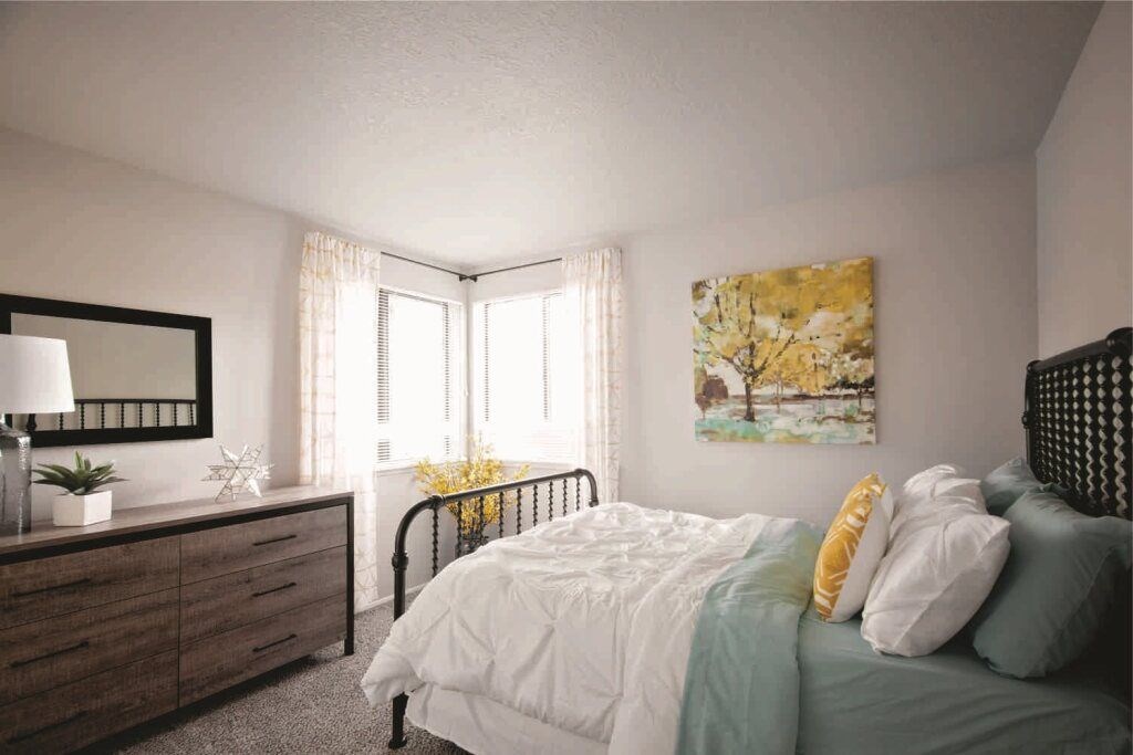 A bedroom with a bed, nightstand, and a painting on the wall.