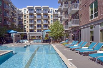 a pool with blue chairs in front of an apartment building