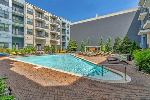 Luxury Apartments in Berry Hill, TN, With In-Unit Washer and Dryer - Octave Apartments - Resort-Style Swimming Pool With Brick Sundeck, Lounge Chairs, Pergola, Green Landscaping, and Apartment Balconies.