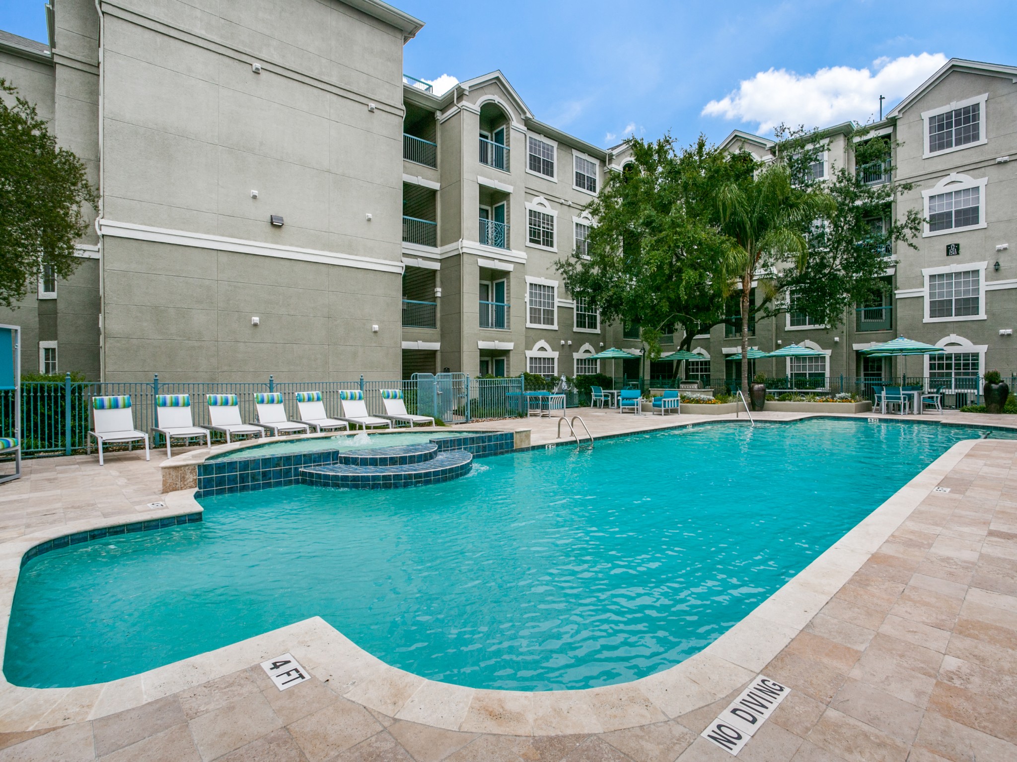 Houston Apartments for Rent - Large Enclosed Community Pool with Lounge Seating Surrounded by Greenery