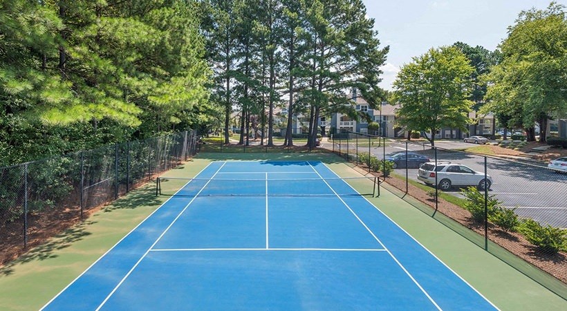 a blue tennis court with trees and a parking lot