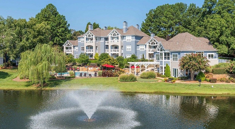 a fountain in a pond in front of a large house